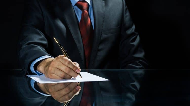 Close up of businessman sitting at table and signing document